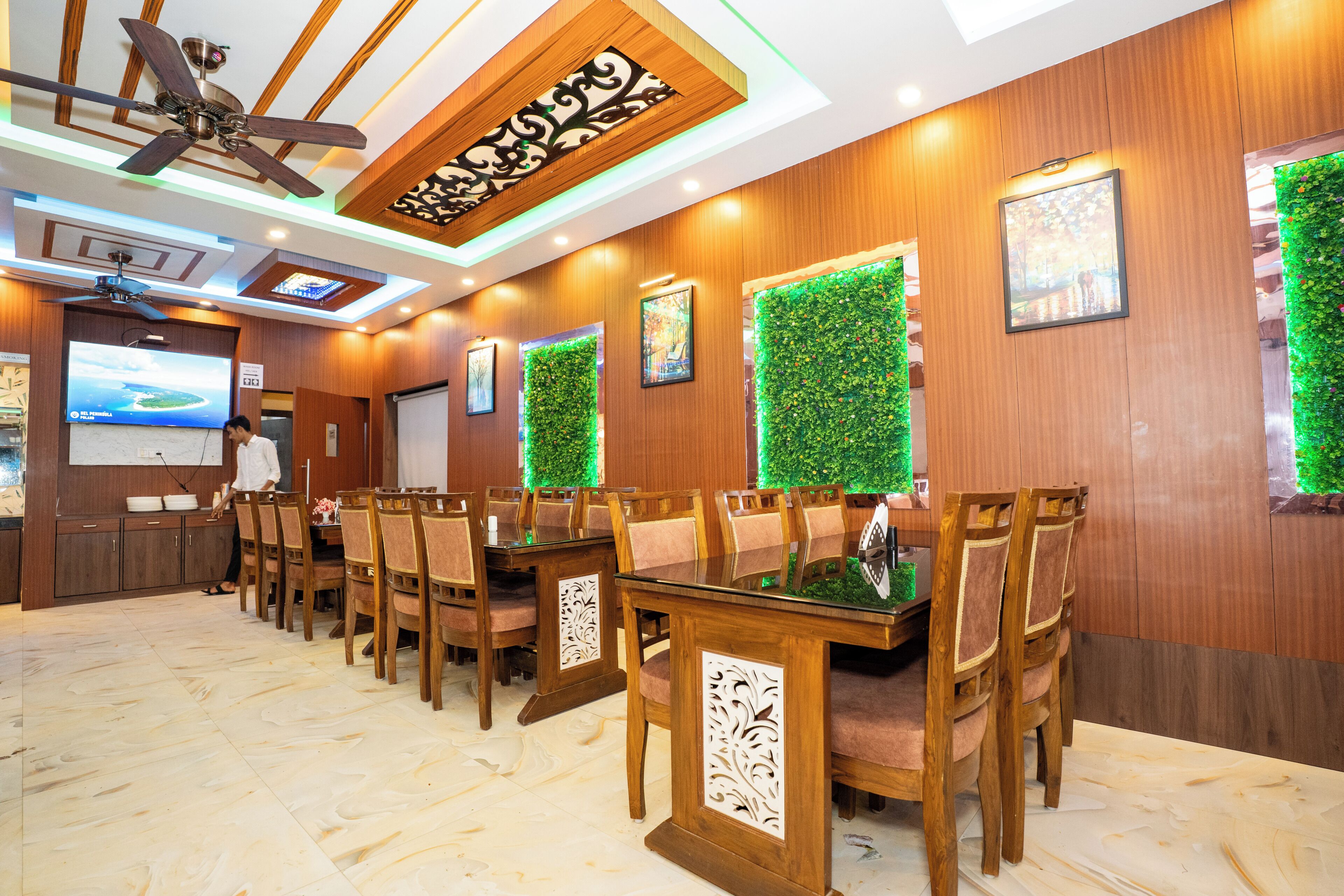 A restaurant with wooden walls, green wall decorations, ceiling fans, and a projection screen.
