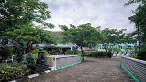Pátio pavimentado com caminho de tijolos, rodeado por vegetação e um edifício com uma placa que diz 'Hotel & Spa Campung'.