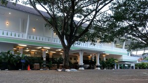 Um hotel com área externa coberta, colunas e uma grande árvore.