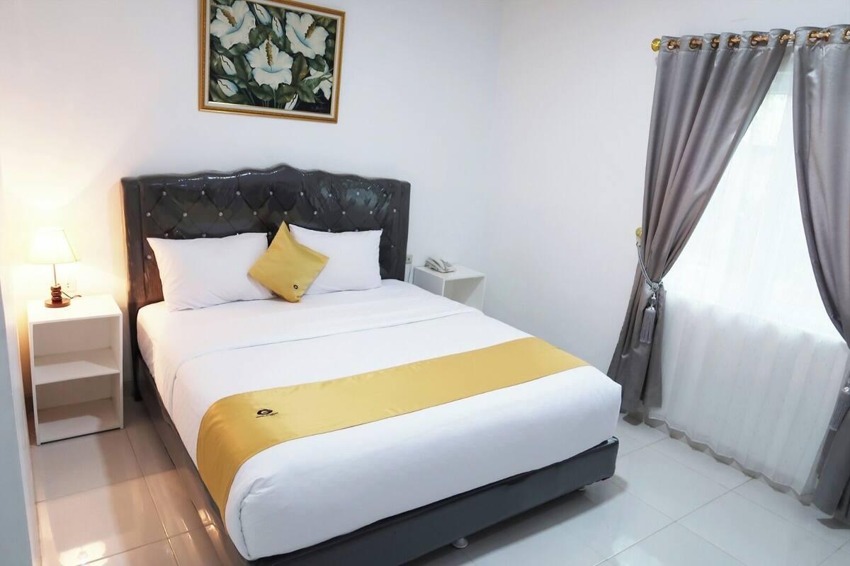 A neatly made bed with a headboard, a bedside table with a lamp, a phone, and a framed picture on the wall.