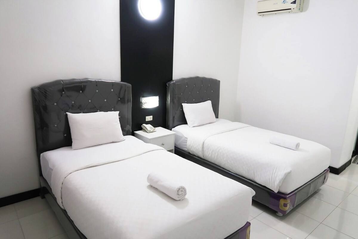 A hotel room with two beds, a nightstand with a phone, and a wall-mounted air conditioner.