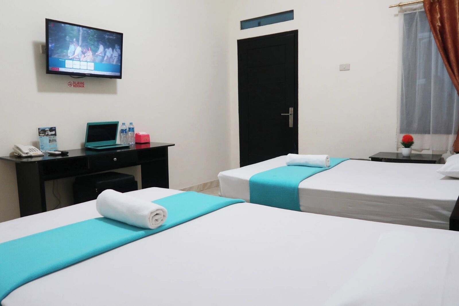 A hotel room with two beds, a desk with a laptop, a TV, and a door.