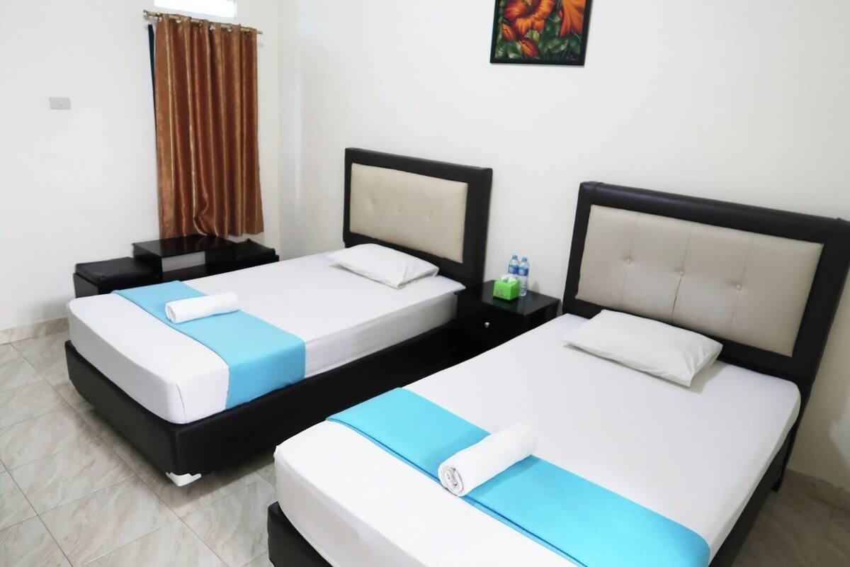 A hotel room with two beds, each with a headboard, a small bedside table, and a nightstand.