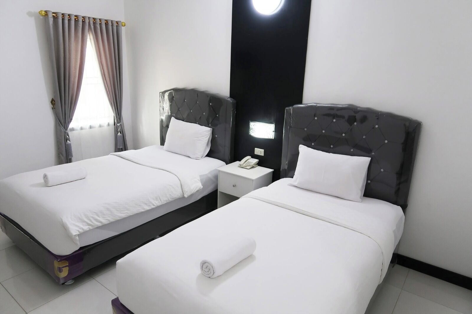 A hotel room with two beds, a nightstand with a phone, and a window with curtains.