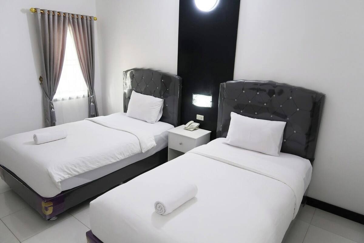 A hotel room with two beds, a nightstand with a phone, and a window with curtains.