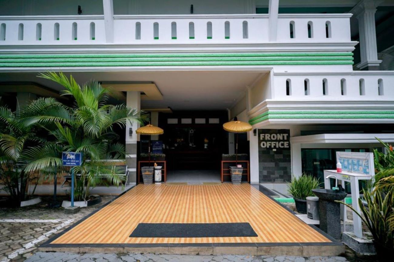 L’entrée d’un hôtel, avec une rampe en bois, des palmiers et un panneau indiquant la réception.