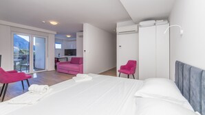 A hotel room with a bed, two pink chairs, a wardrobe, and a balcony with a view. - Altiora Prestige Residence 105 (Gradac)