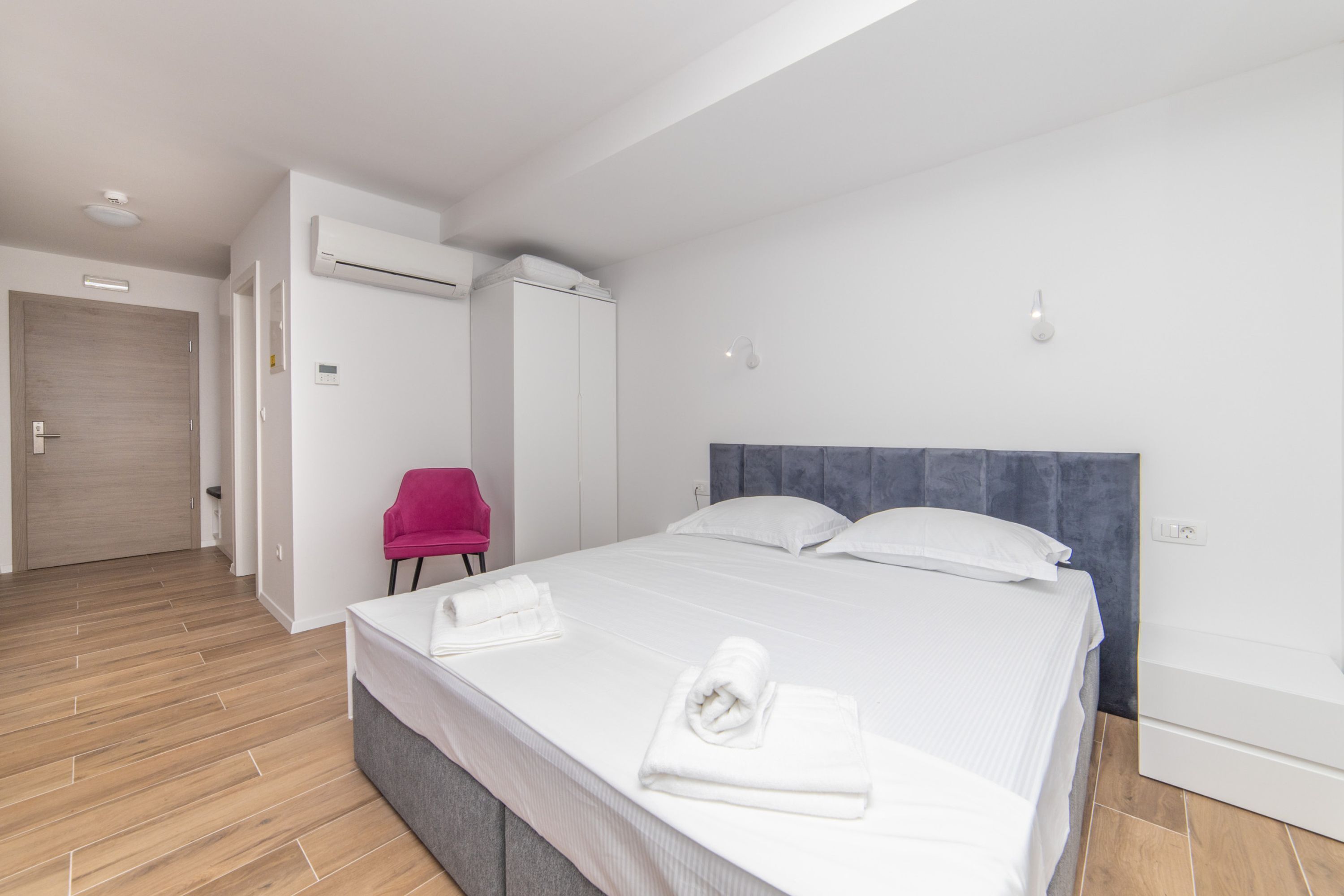 Una habitación de hotel moderna con una cama grande, un armario, una silla y un equipo de aire acondicionado.