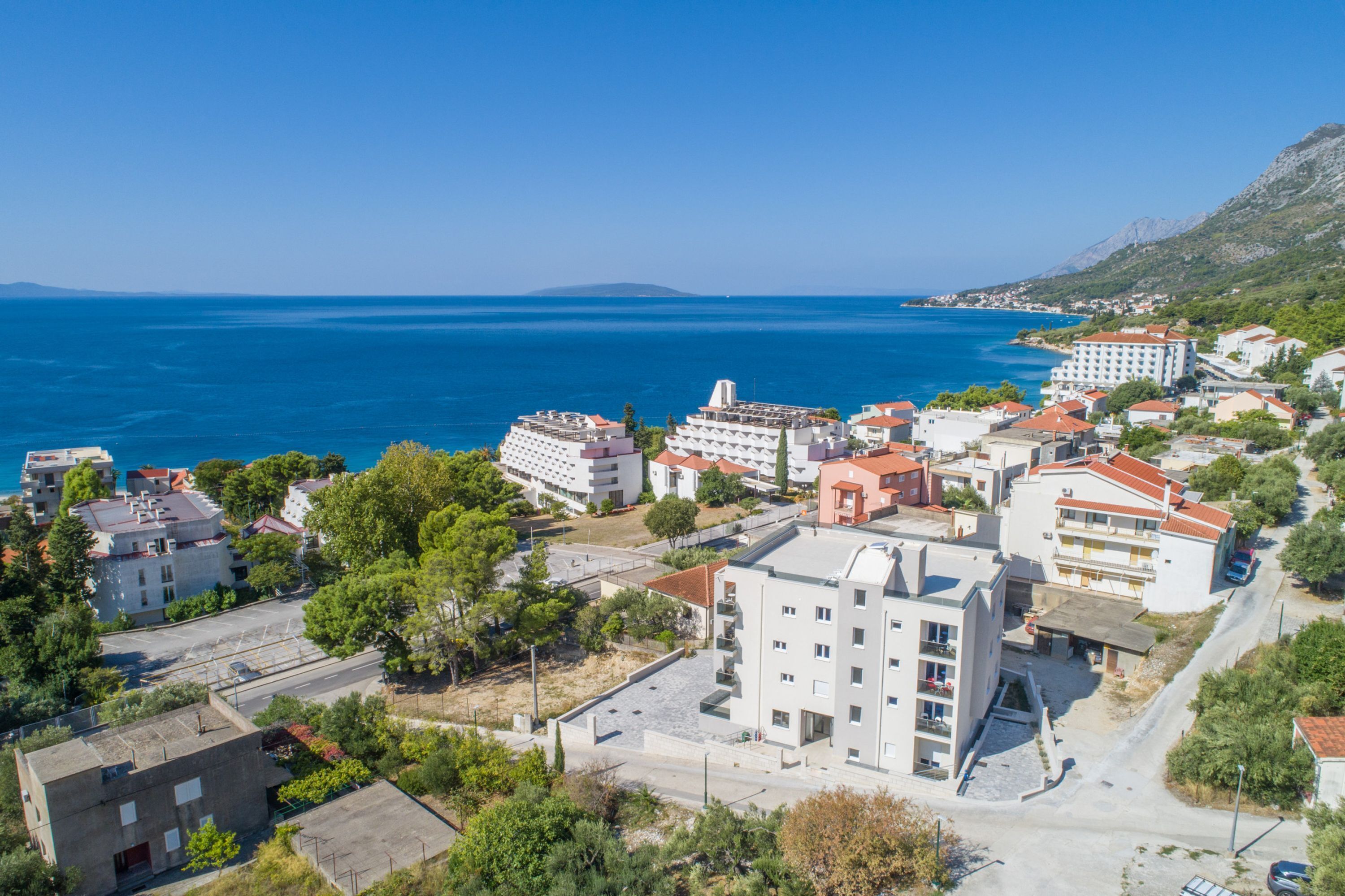 Une ville côtière avec des bâtiments, une mer d’un bleu limpide et un paysage vallonné en arrière-plan.