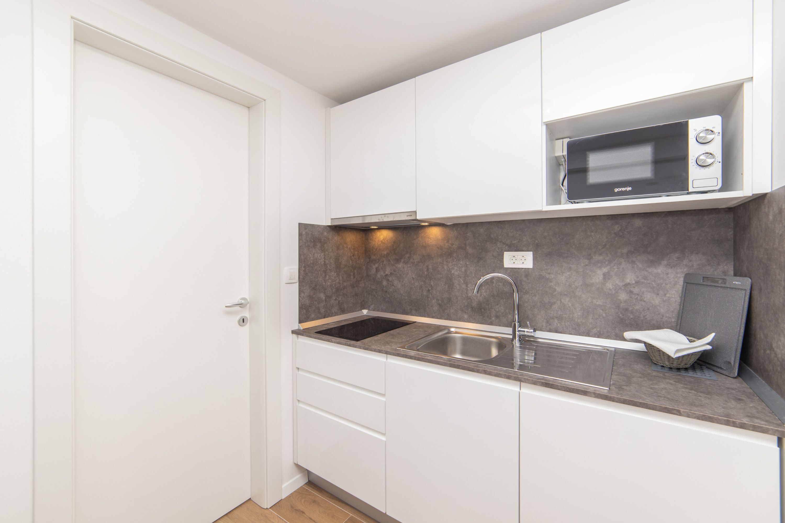 A compact kitchen with white cabinets, a stainless steel sink, a microwave, and a built-in scale.