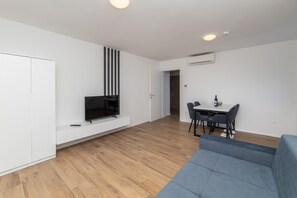A modern living space with a flat-screen TV on a built-in shelf, a dining area with a table and chairs, and a grey sofa. - Altiora Prestige Residence 301 (Gradac)