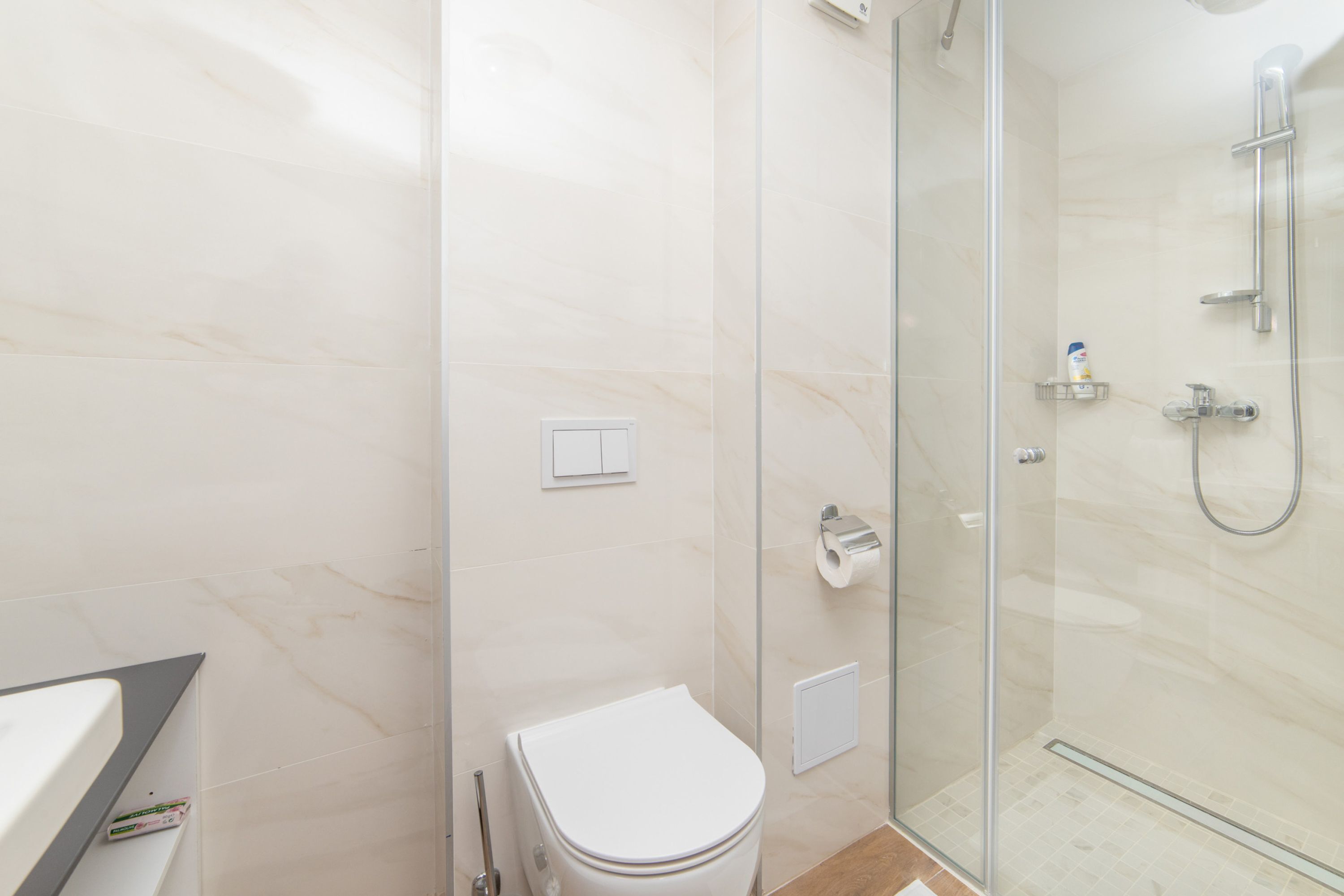 A bathroom with a toilet, a glass shower enclosure, and a marble-tiled wall.