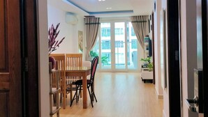 A spacious room with a wooden floor, a dining table with chairs, a ceiling light, and a view through large windows. - Luxury 2 bedroom Apartment Sky Center (Ho Chi Minh City)