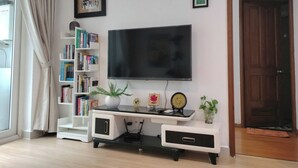 A living room with a flat-screen TV, a bookshelf, a small plant, and a door. - Luxury 2 bedroom Apartment Sky Center (Ho Chi Minh City)
