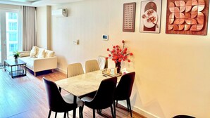 A modern living room with a sofa, dining table, chairs, and a vase with red flowers. - Luxury 2 bedroom Apartment Sky Center (Ho Chi Minh City)