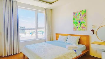 A modern bedroom with a large bed, a window with curtains, a painting on the wall, and a bedside table with a lamp.