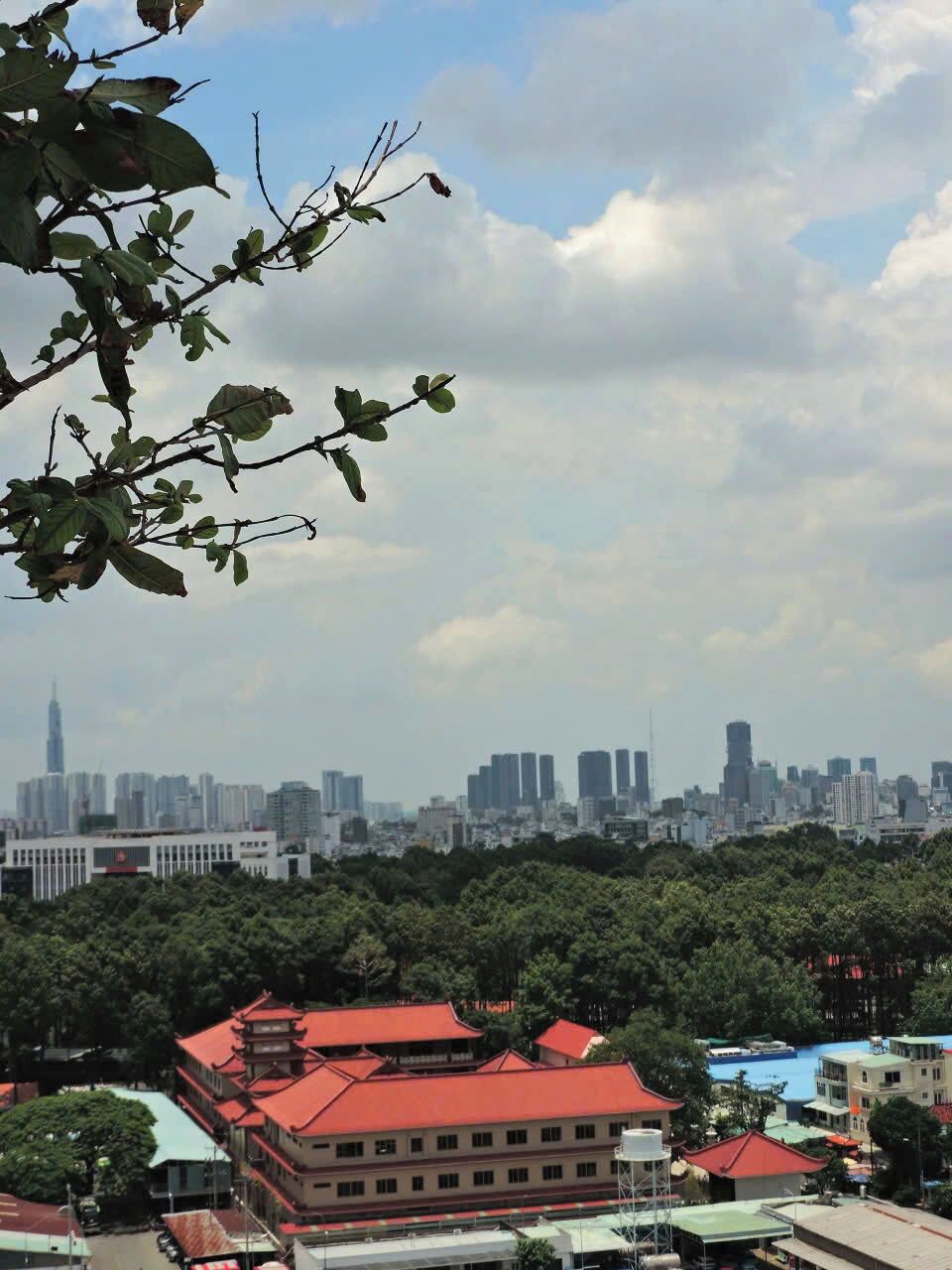 A cityscape with a prominent building in the distance, surrounded by dense greenery and a clear sky.