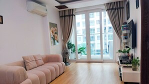 A living room with a sofa, a standing fan, a potted plant, and a window with curtains. - Luxury 2 bedroom Apartment Sky Center (Ho Chi Minh City)
