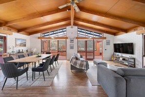 A spacious living area with a high ceiling, a dining table, sofas, and a television. - Multi-Family Coastal Escape | Camp & Stay (St Leonards)