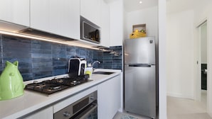 A modern kitchen with a stainless steel refrigerator, a gas stove, and white cabinetry. - CASA APREDA (Sorrento)