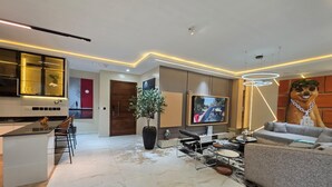 A modern living room with a flat-screen TV, a sofa, a coffee table, and a dining area with chairs. - Primehomes  (Lekki)
