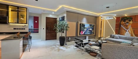Een moderne woonkamer met een flatscreen televisie, een bank, een salontafel en een eethoek met stoelen.