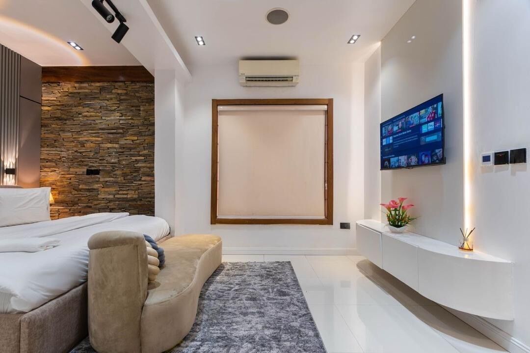 A modern bedroom with a stone wall, a bed, a sofa, a TV, and a wall-mounted air conditioner.