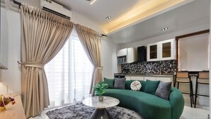 A modern living room with a green sofa, a round coffee table, and a kitchen area in the background. - Primehomes  (Lekki)