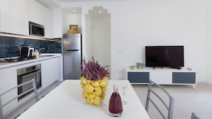 A modern kitchen with white cabinets, a stainless steel refrigerator, a microwave, and a dining area with a white table and chairs. - Stayxperience - Casa Apreda (Sorrento)