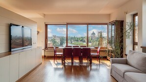 A spacious living area with a dining table and chairs, a sofa, a flat-screen TV mounted on the wall, and large windows offering a city view. - Residenza vista mozzafiato Ponte Pietra (Verona)