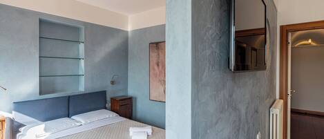 A bedroom with a bed, a nightstand, a mirror, and a built-in shelf.