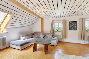Una sala de estar moderna con techo inclinado, un sofá modular, una mesa de centro y un ventanal con cortinas.