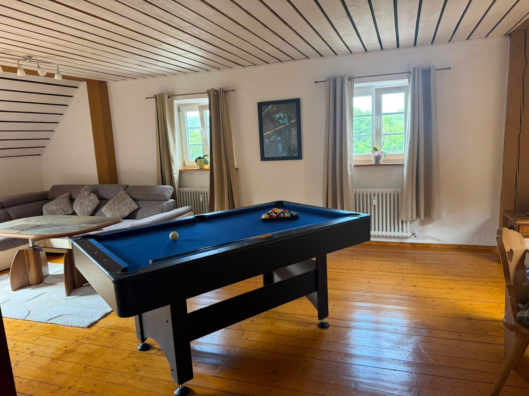 Une pièce avec une table de billard, un canapé et une fenêtre avec des rideaux.