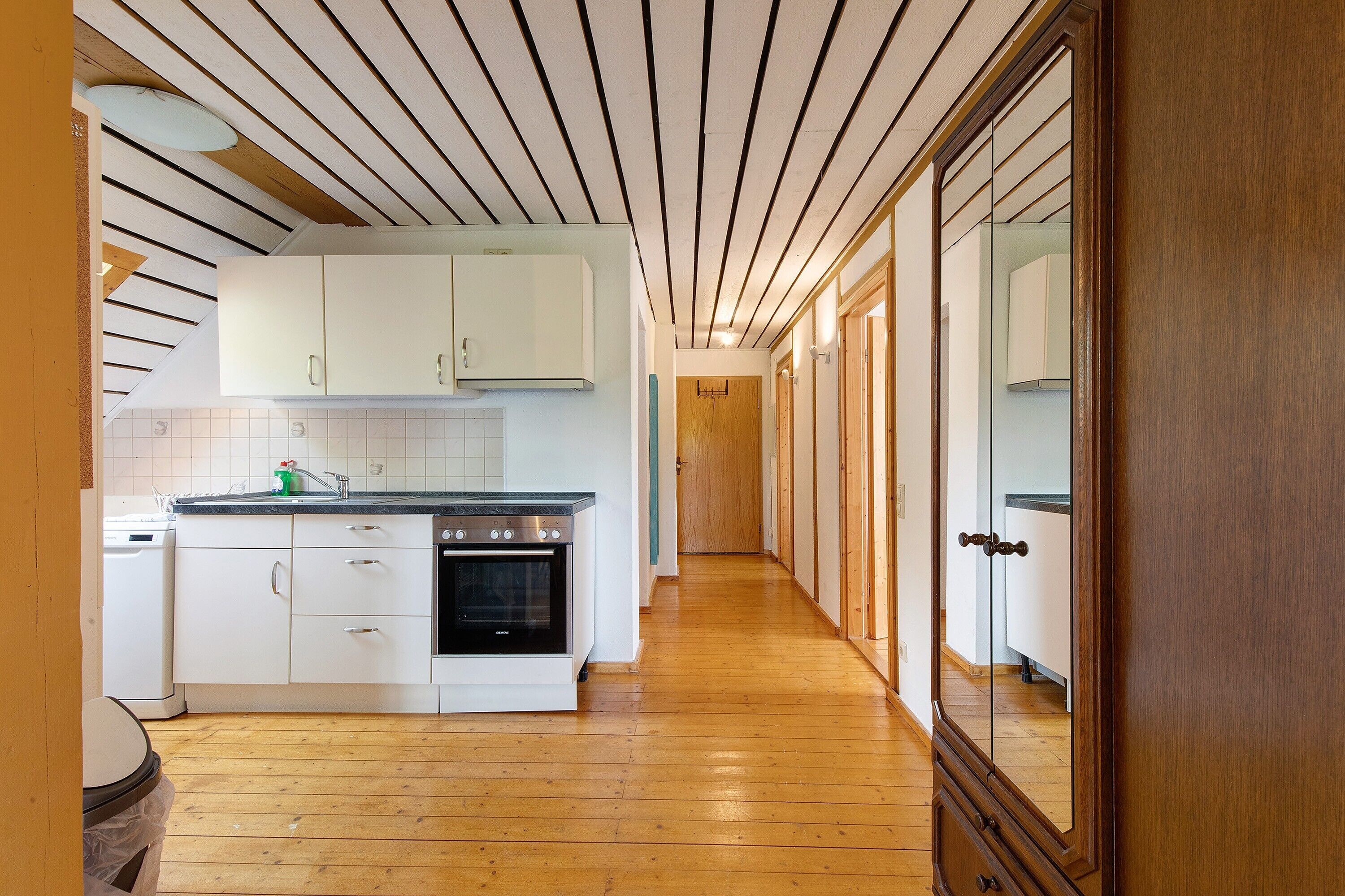 A kitchen with wooden flooring, white cabinets, a stove, and a wooden door.