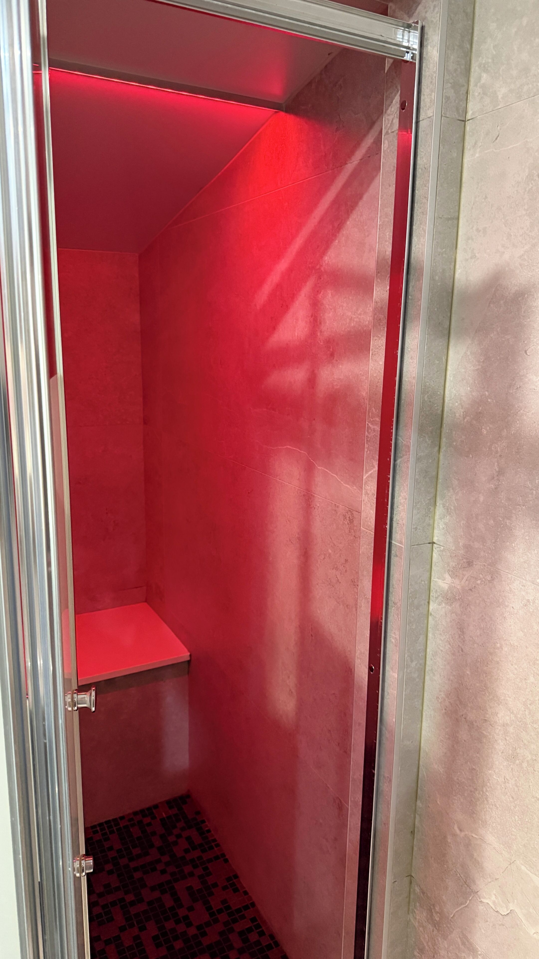 Um espaço pequeno e fechado, com decoração vermelha, porta de metal e chão de azulejos.