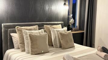 Een net opgemaakt bed met een gestreept dekbedovertrek, meerdere kussens en een opgerolde handdoek op een houten vloer.