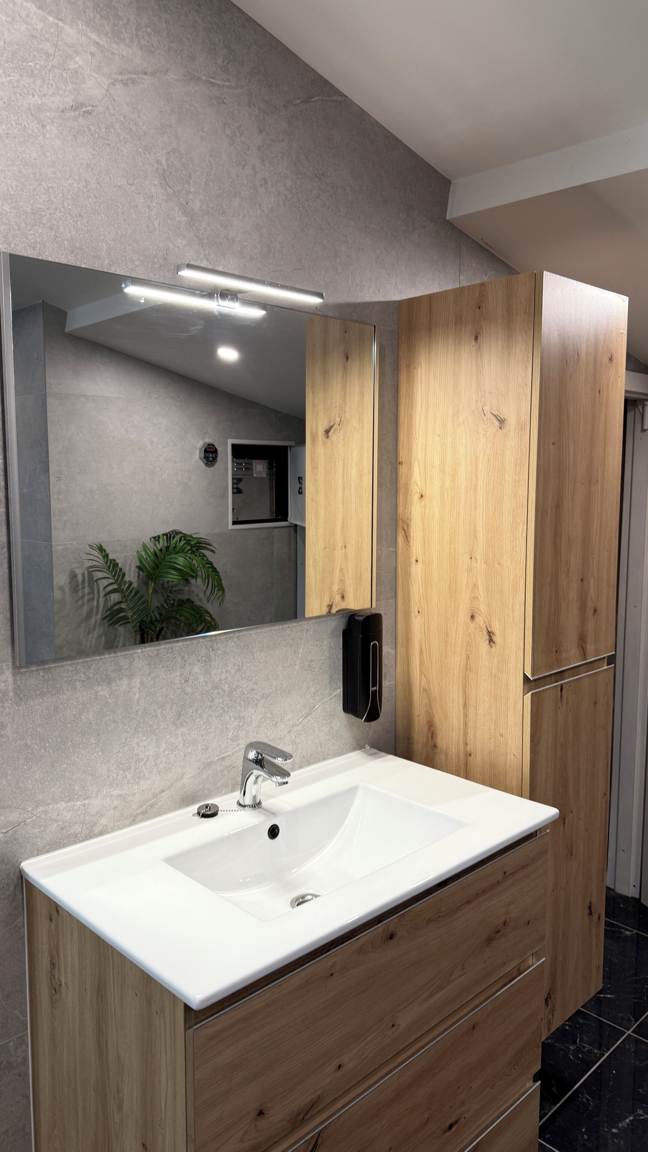 Een moderne badkamer met een grote spiegel, een witte wastafel, houten kastjes en een douche.