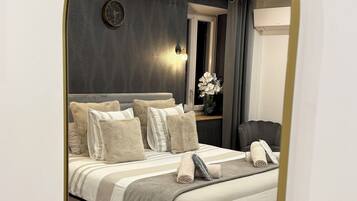 A bedroom with a bed, pillows, a bedside table, a mirror, and a window.