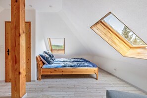 A bedroom with a sloped ceiling, a wooden bed, a skylight, and a door.