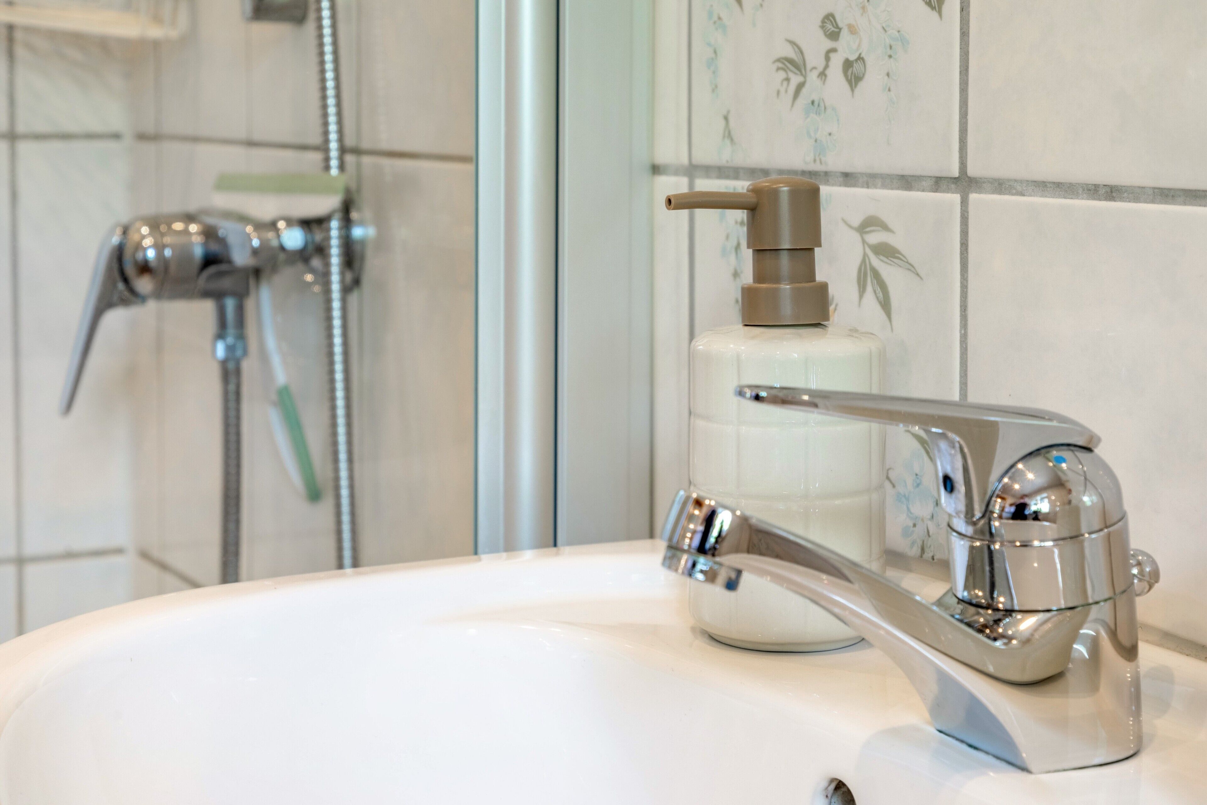 A bathroom with a chrome faucet, a soap dispenser, and a showerhead.