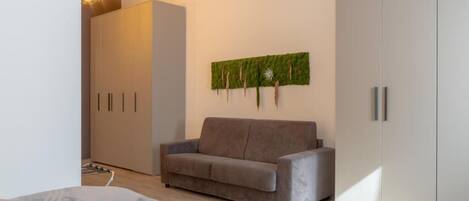 A modern bedroom with a grey sofa, a wardrobe, and a wall-mounted artwork.