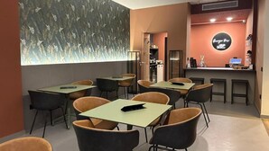 A modern cafe with tables and chairs, a counter with a neon sign, and a decorative wall.