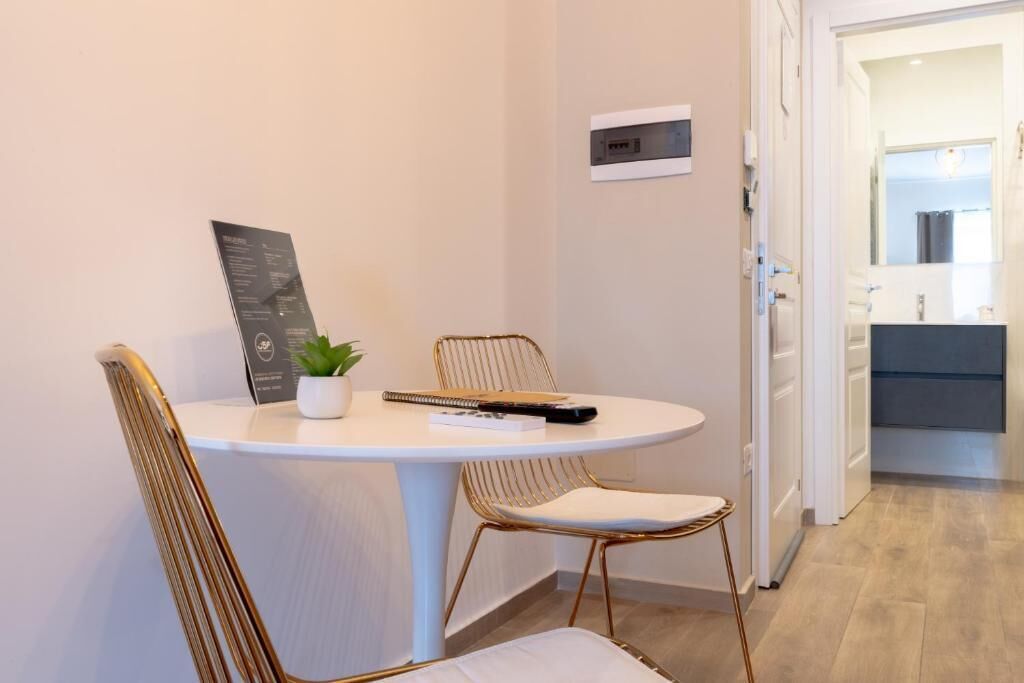 A small dining area with a round table, two chairs, a potted plant, and a remote control.