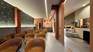 A hotel lobby with rows of chairs, a reception desk, and a wall with a leaf pattern.