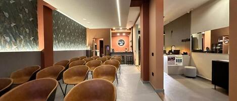 A hotel lobby with rows of chairs, a reception desk, and a wall with a leaf pattern.