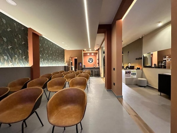 A hotel lobby with rows of chairs, a reception desk, and a wall with a leaf pattern.