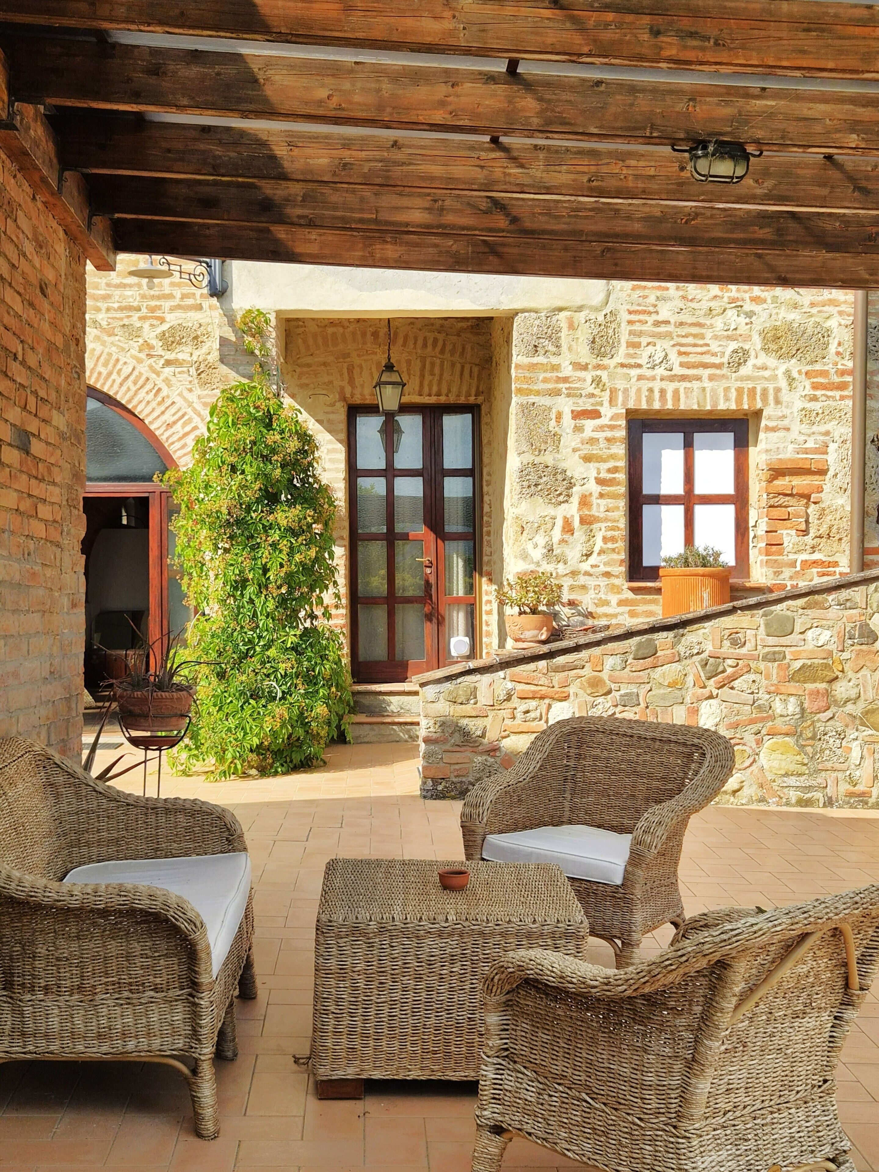 A covered outdoor seating area with wicker furniture, a stone wall, and a wooden ceiling.