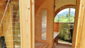 A wooden sauna room with a bench, a glass door, and a view of greenery outside.