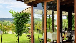 A covered patio with a table and chairs, surrounded by potted plants and a view of the countryside.