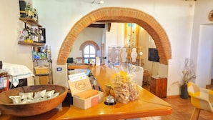 A rustic interior with a wooden counter, a brick archway, and various items like a bowl, packaged goods, and a sign.